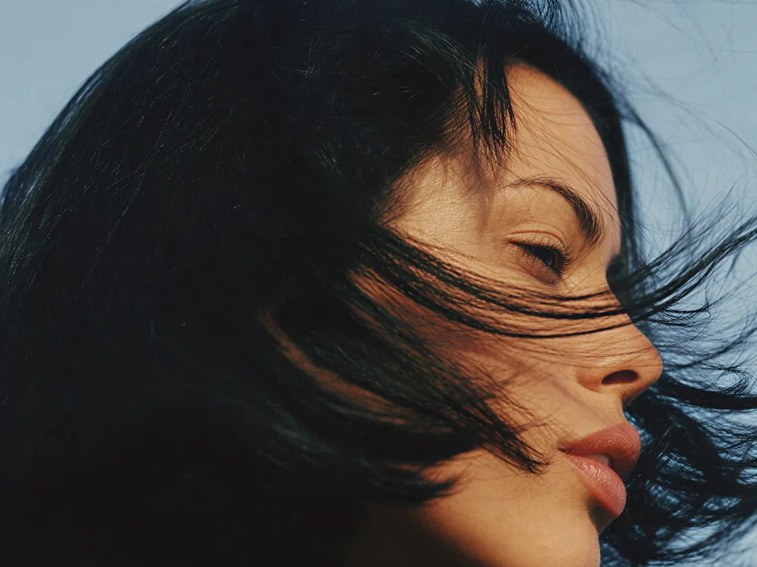 A woman in natural daylight with her hair moving in the wind, calm and unhurried